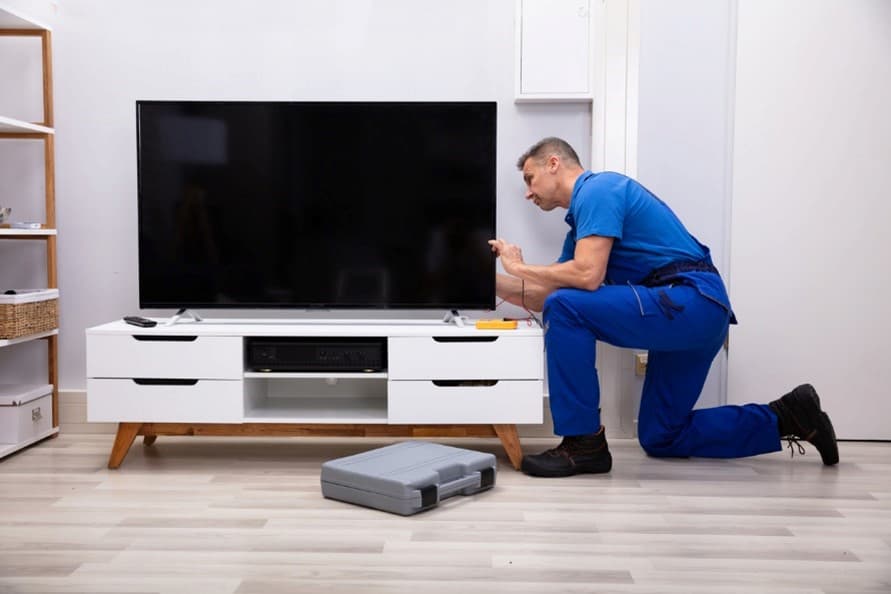 A person in blue uniform kneeling next to a tv